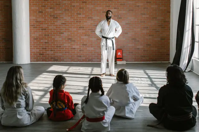 Classe d'arts marcials en un dojo lluminós: l'instructor davant del grup, assegut a terra